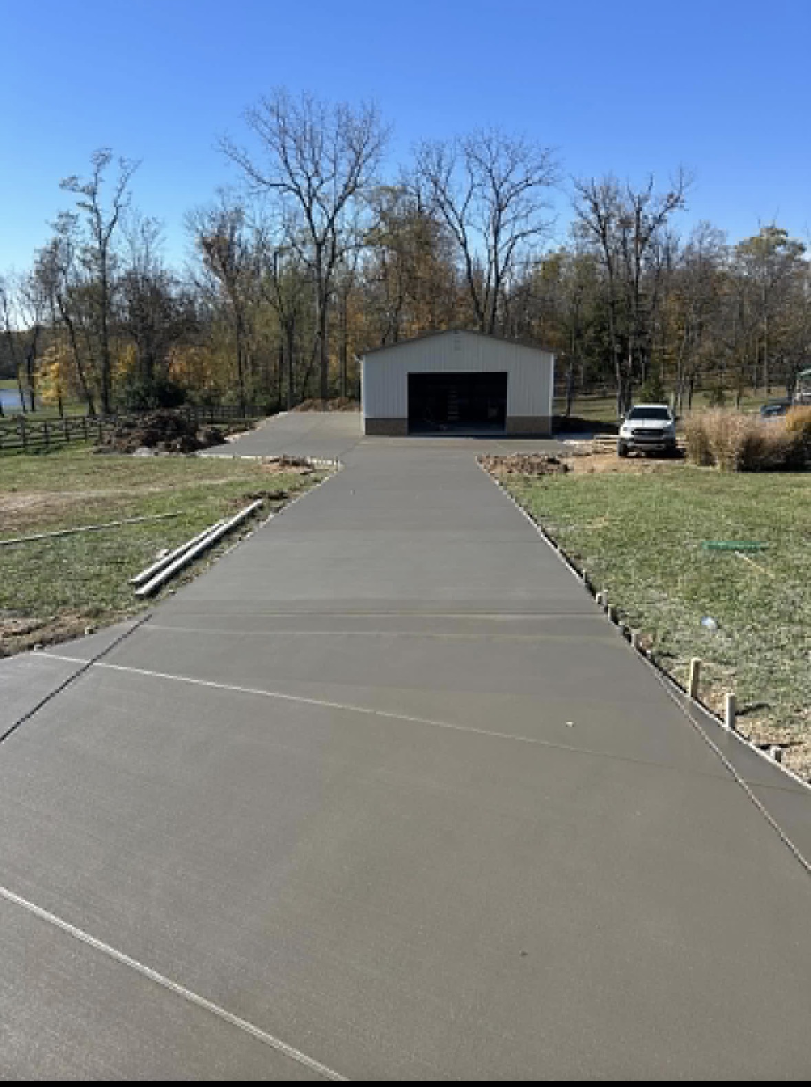 Freshly poured concrete driveway leading to a finished pole barn